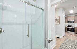 A glass shower door in a white bathroom at The Ashton at East Park Apartments, Kennesaw, 30144