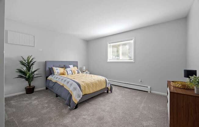 A bedroom with a bed, a plant, and a window.