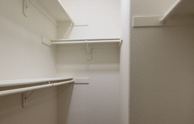 a walk in closet with white walls and shelves and a wood floor