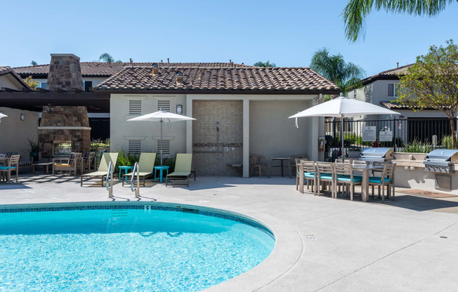 a swimming pool in front of a house with tables and umbrellas