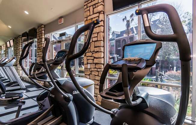 A row of treadmills in a gym with a view of the outside.