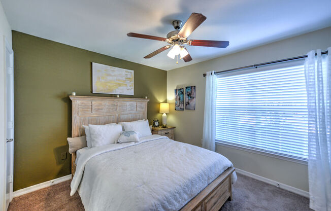 A bedroom with a bed, a ceiling fan, and a window with blinds.