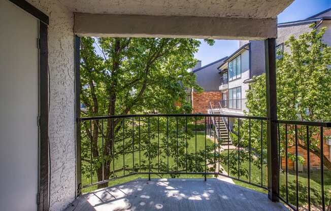 A balcony with a metal railing overlooks a green lawn and trees.