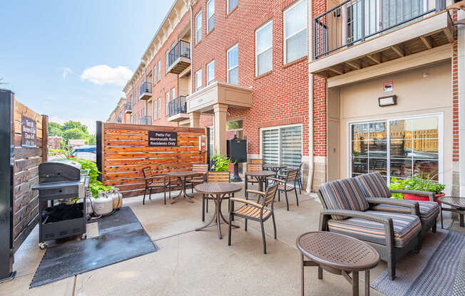 A patio with a grill and chairs is surrounded by a brick building.