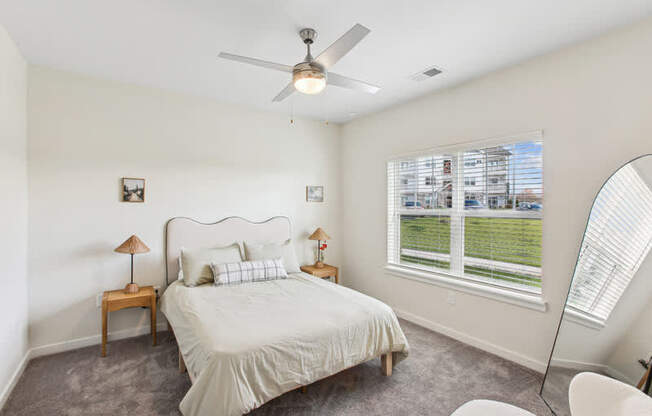A bedroom with a large bed, a ceiling fan, and a window with blinds.