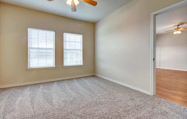 an empty living room with two windows and a ceiling fan