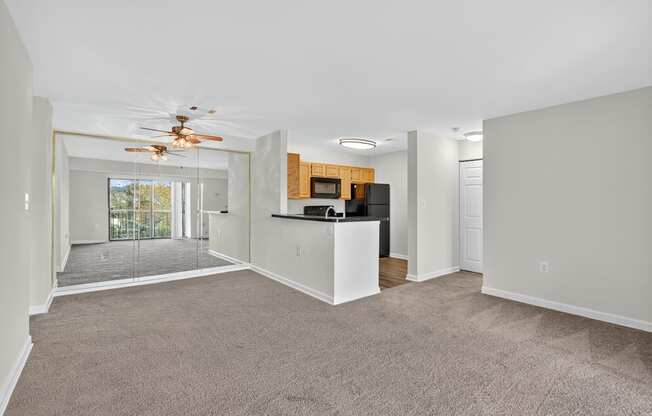 A spacious living room with a ceiling fan and a kitchen in the background.
