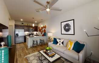 a living room with a couch and coffee table in front of a kitchen with a breakfast bar