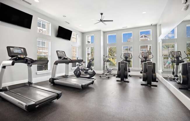 the gym with treadmills and other exercise equipment in a building with windows