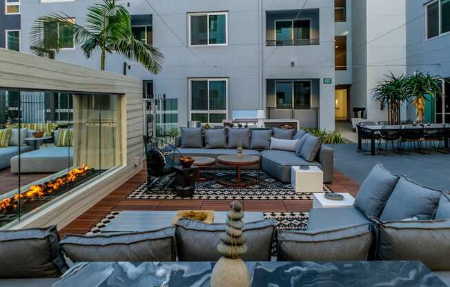 A modern outdoor seating area with grey couches and a fire pit.