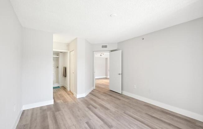 A room with white walls and wooden flooring with a door on the right.