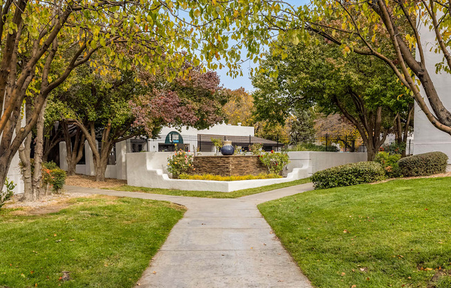 a sidewalk leading to a house with trees and a fountain