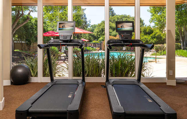 Two treadmills are in a room with a view of the backyard.