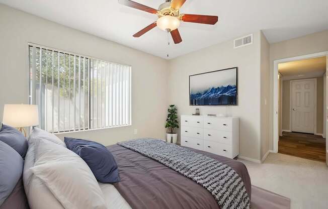A bedroom with a bed, a ceiling fan, and a painting on the wall.