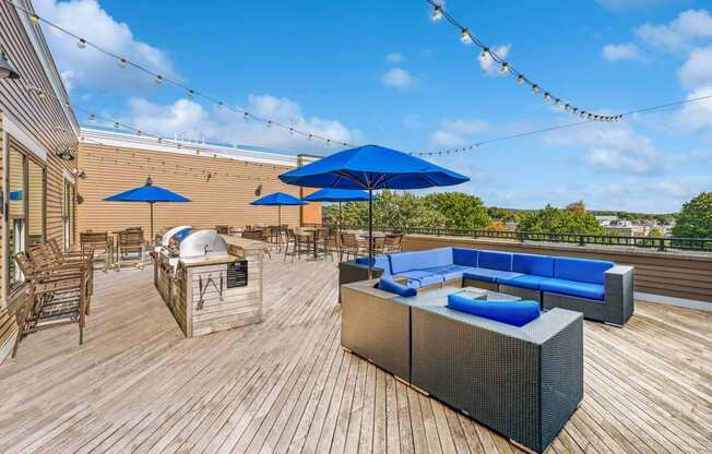 a patio with blue umbrellas and furniture on a roof at The Merc, Waltham, MA, 02453