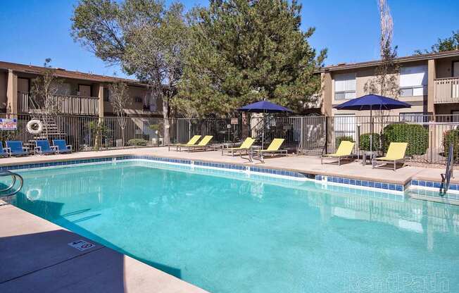 A swimming pool with a blue umbrella and yellow chairs.