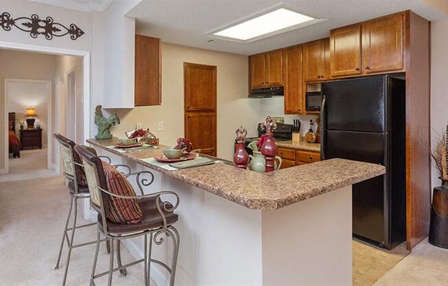 a kitchen with a bar with three chairs at Bedford Parke Apartments, Warner Robins, GA
