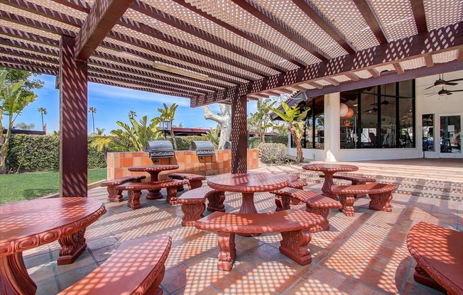 a patio with tables and benches and a pool in the background