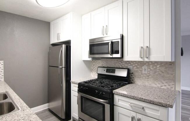 Kitchen with quartz stone counters and stainless steel microwave, oven, fridge, and fixtures.