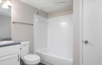 A white toilet sits next to a white bathtub in a small bathroom.