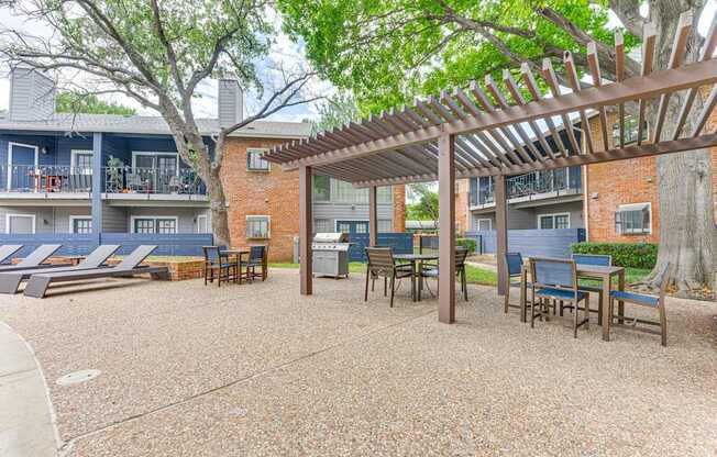 A patio with a pergola and chairs is surrounded by apartment buildings.