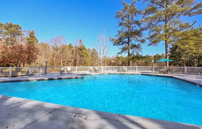 A large swimming pool surrounded by a white fence and trees.