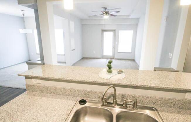 View from kitchen counter with sink with a living room with a door and window in the background at Mosaic Apartments in Avon, Indiana