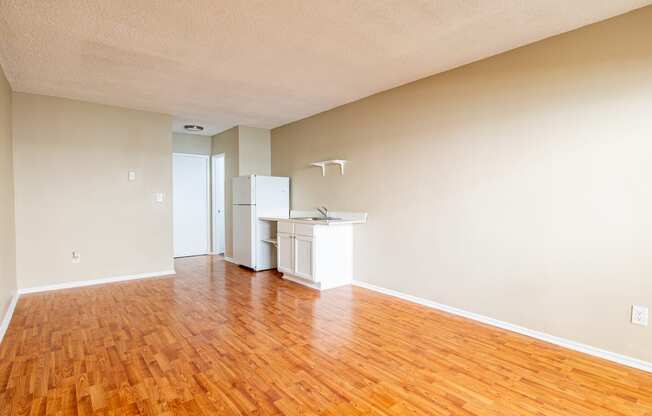 an empty living room with wood floors and a kitchen