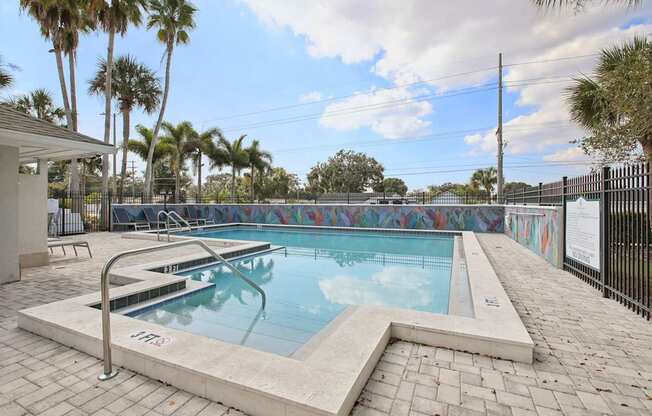 A pool surrounded by palm trees and a fence.