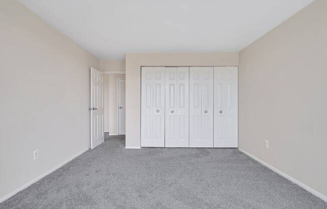 an empty bedroom with white closets and carpeting