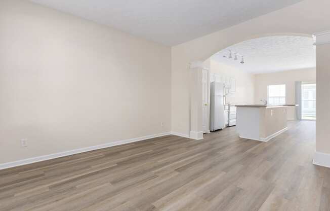 an empty living room and kitchen with white walls and wood flooring