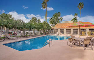 A pool with chairs and a building in the background.