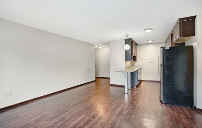 an empty living room and kitchen with wood flooring and a refrigerator