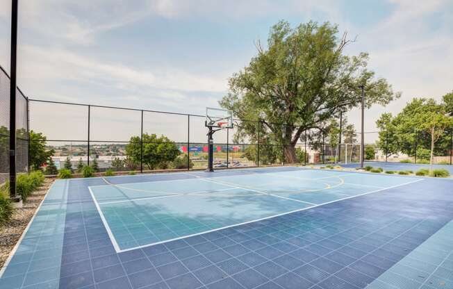 a blue basketball court with trees and a fence