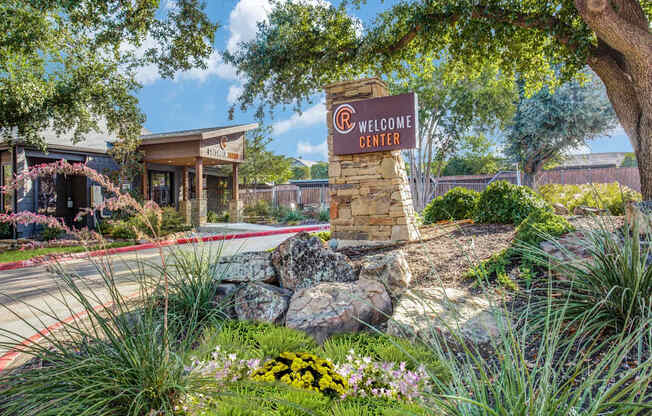 A welcome center sign is in front of a building with a landscaped area.
