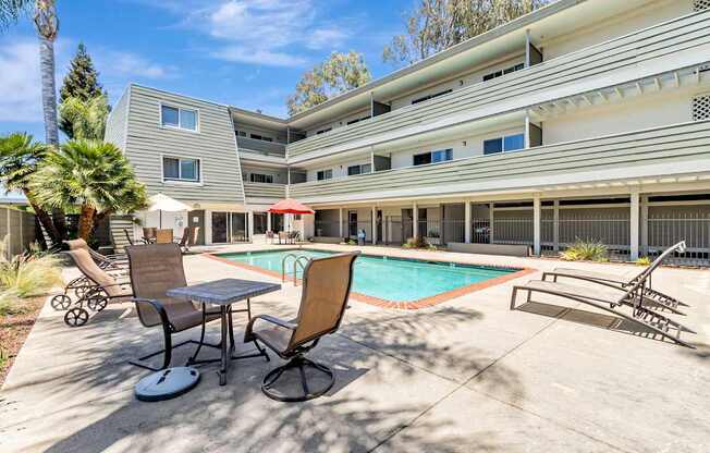 A pool area with chairs and a table in front of a building.