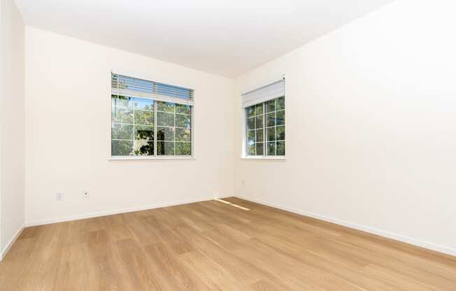 a bedroom with white walls and wood floors and two windows