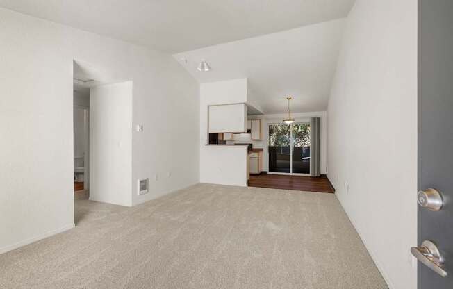 A large, empty room with a carpeted floor and a door on the right side at Clackamas Trails Apartments, Oregon, 97222
