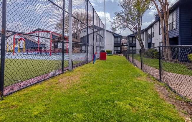 a fenced in grassy area with a playground next to a chain link fence