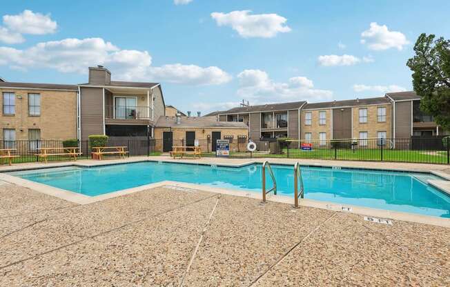A swimming pool surrounded by a stone patio and apartment buildings.