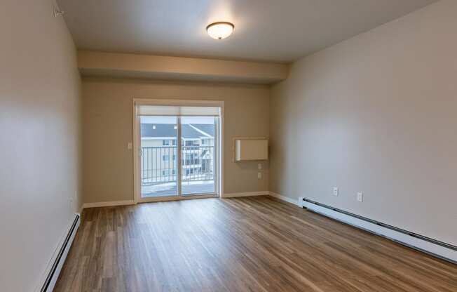 an empty living room with wood flooring and a door to a balcony. Fargo, ND Prairiewood Meadows