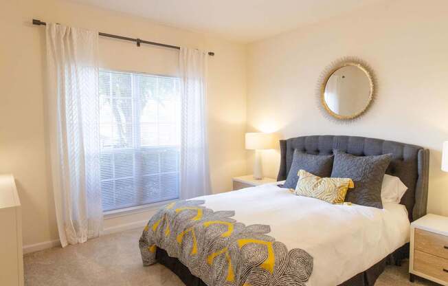 A bedroom with a large bed and a round mirror on the wall.