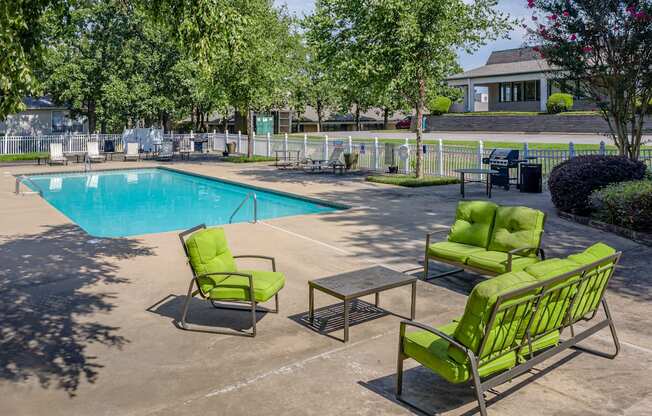 a swimming pool with green chairs and tables around it