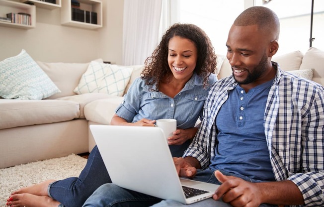 a man and woman sitting on the floor using a laptop computer