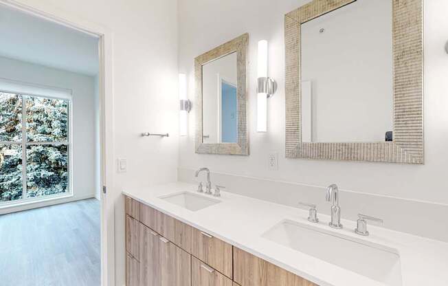 A bathroom with a large mirror and a window overlooking a snowy landscape at One West Drive Apartments, Excelsior