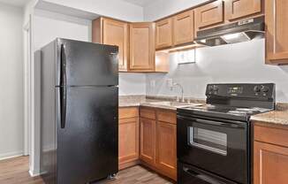 A black refrigerator stands in a kitchen with wooden cabinets.