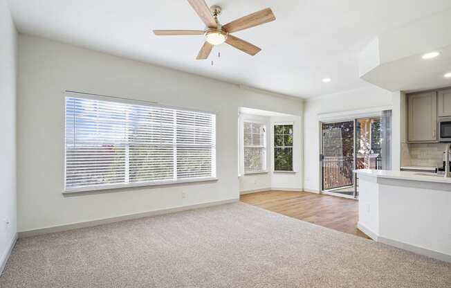 an empty living room with a ceiling fan and a kitchen