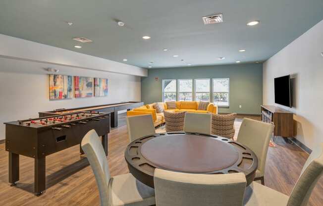 Room with a table, chairs, foosball and shuffle board table, a couch and tv at The Vue Luxury apartments in Indianapolis