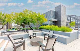 A patio with chairs and a table is surrounded by trees.