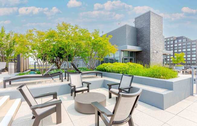 A patio with chairs and a table is surrounded by trees.